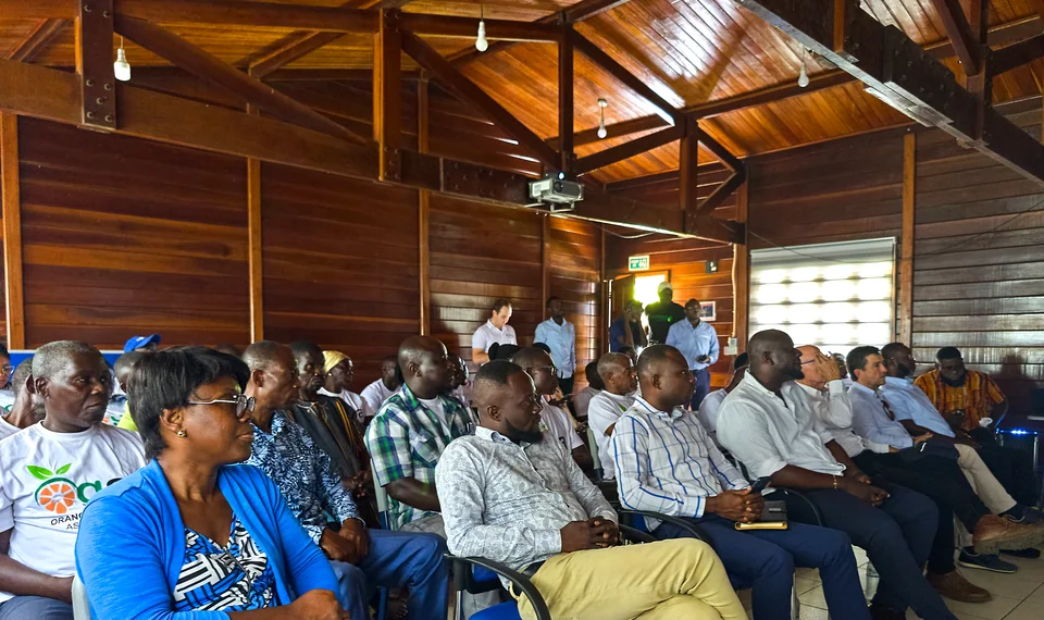People seated at a meeting in a wooden hall.