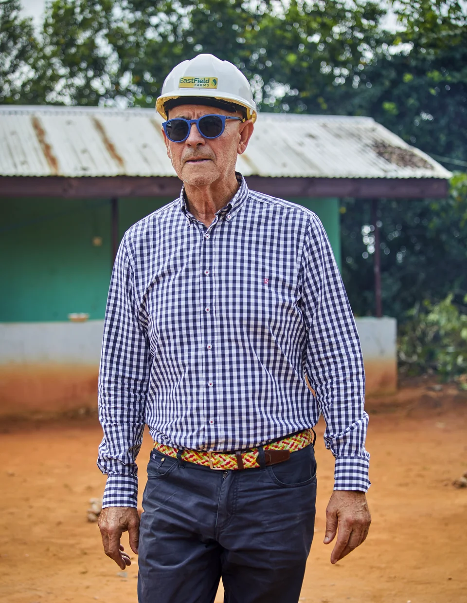 A visitor in a hard hat and sunglasses outside a farm building.
