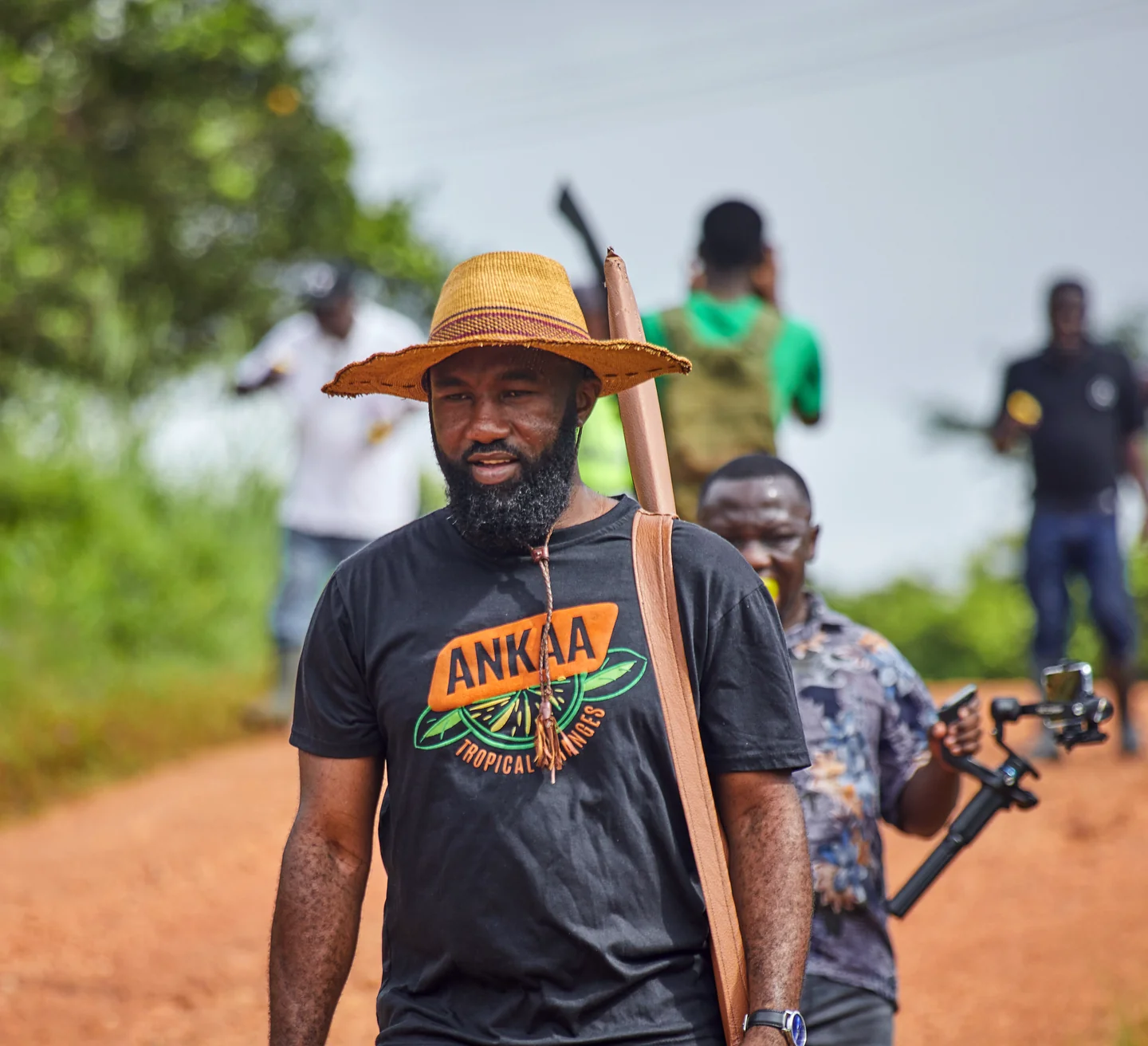A man in a straw hat walks a red dirt farm road, with others behind him.