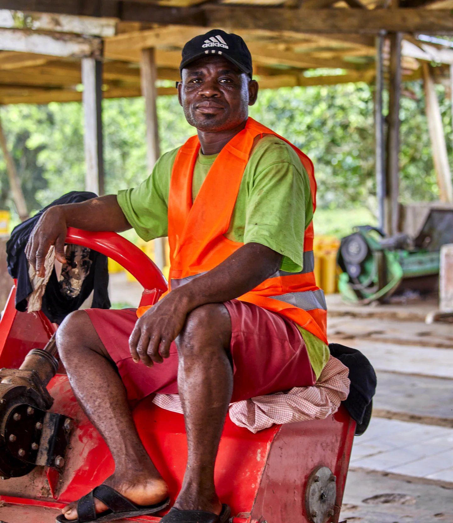 A worker in an orange safety vest sits on a red machine at the packing shed.